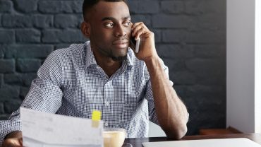 Handsome confident African-American businessman doing paperwork, studying invoice in his hand and ta