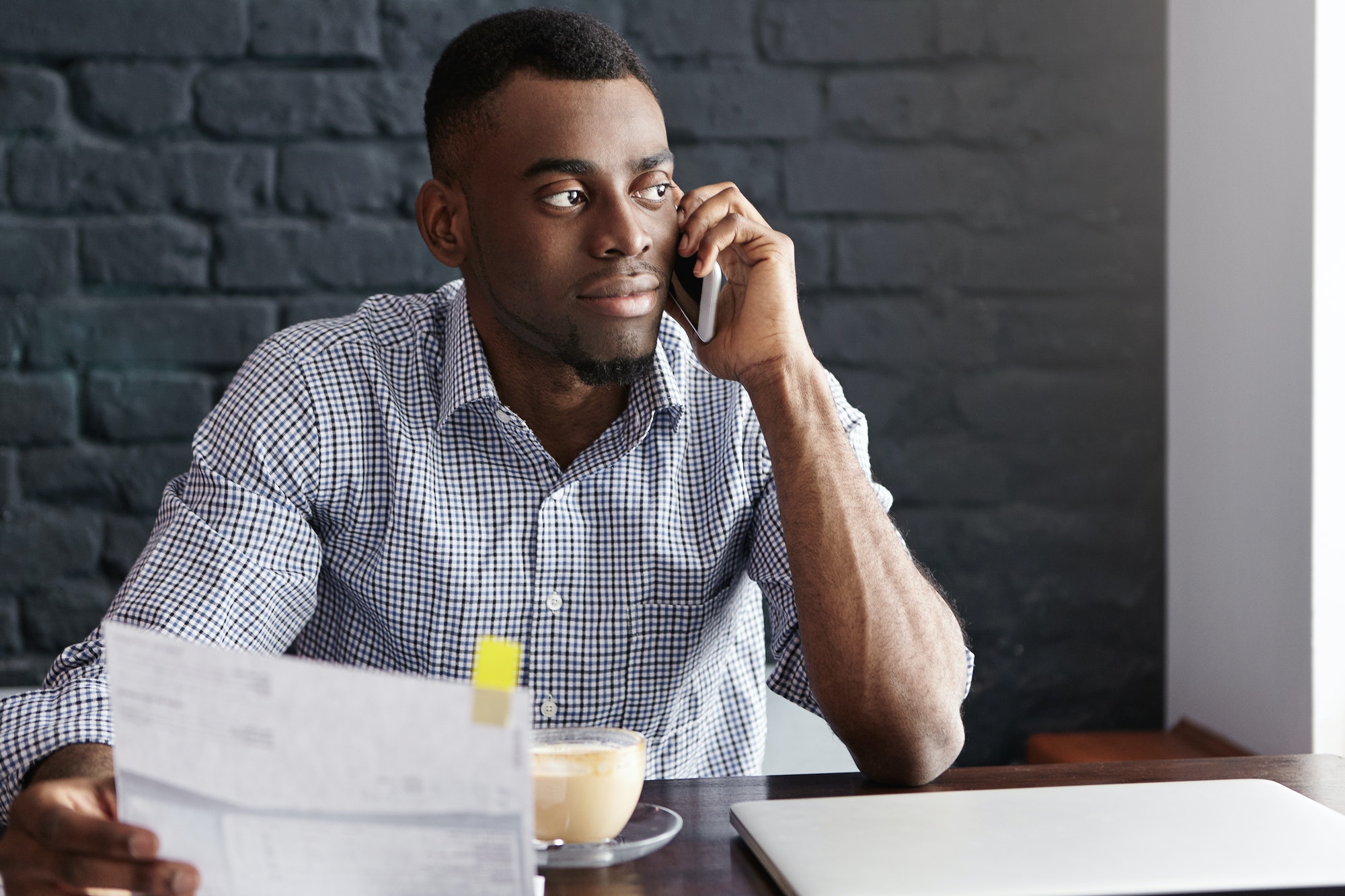 Handsome confident African-American businessman doing paperwork, studying invoice in his hand and ta