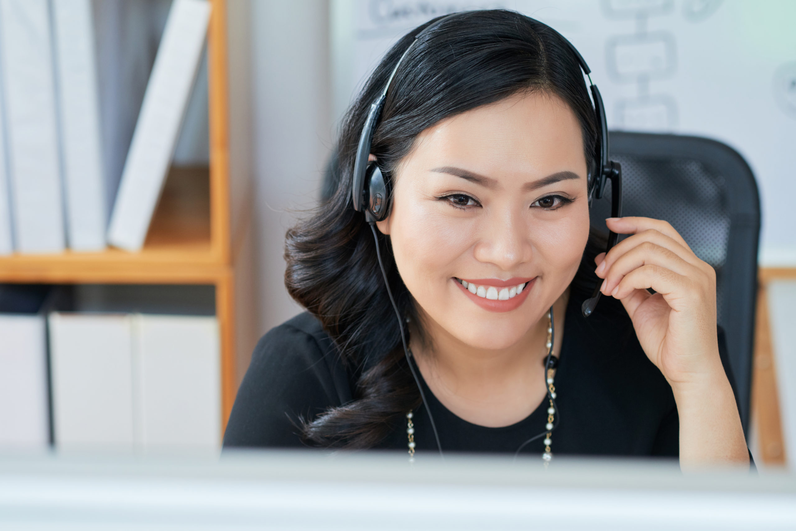 Attractive Asian businesswoman in headset reading data on computer screen