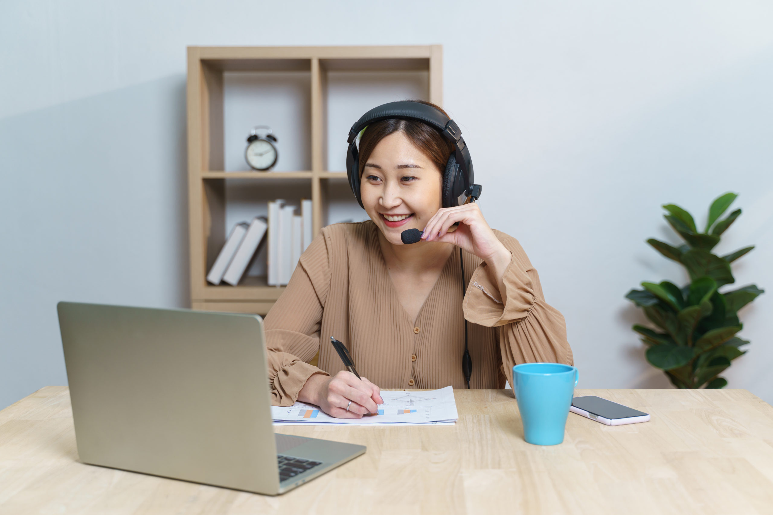 Young adult Asian female student using headset listen on laptop screen learning online courses. Chinese business woman wear headphones working with computer as video call for customer service